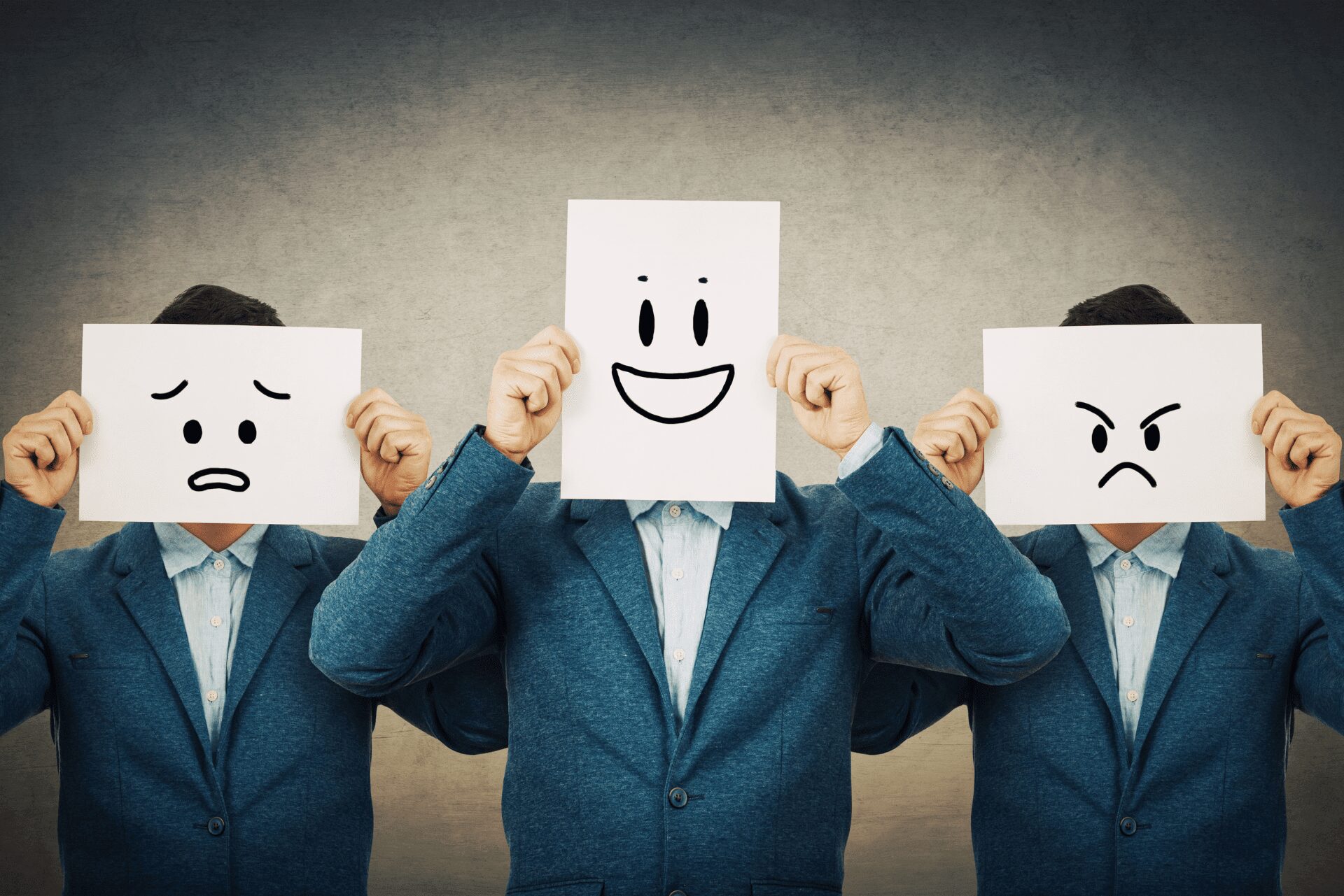 Trois personnes en costume tiennent des pancartes représentant différentes émotions — une métaphore visuelle pour apprendre à comprendre ses émotions.
