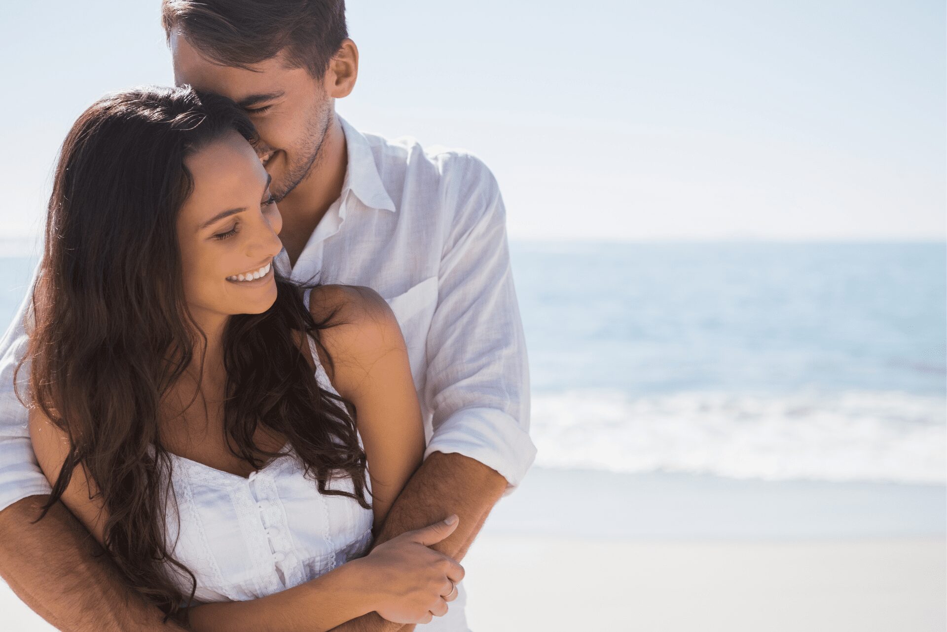 Couple souriant s’enlaçant sur la plage, illustrant la loi de l’attraction et la manifestation d’une relation harmonieuse.