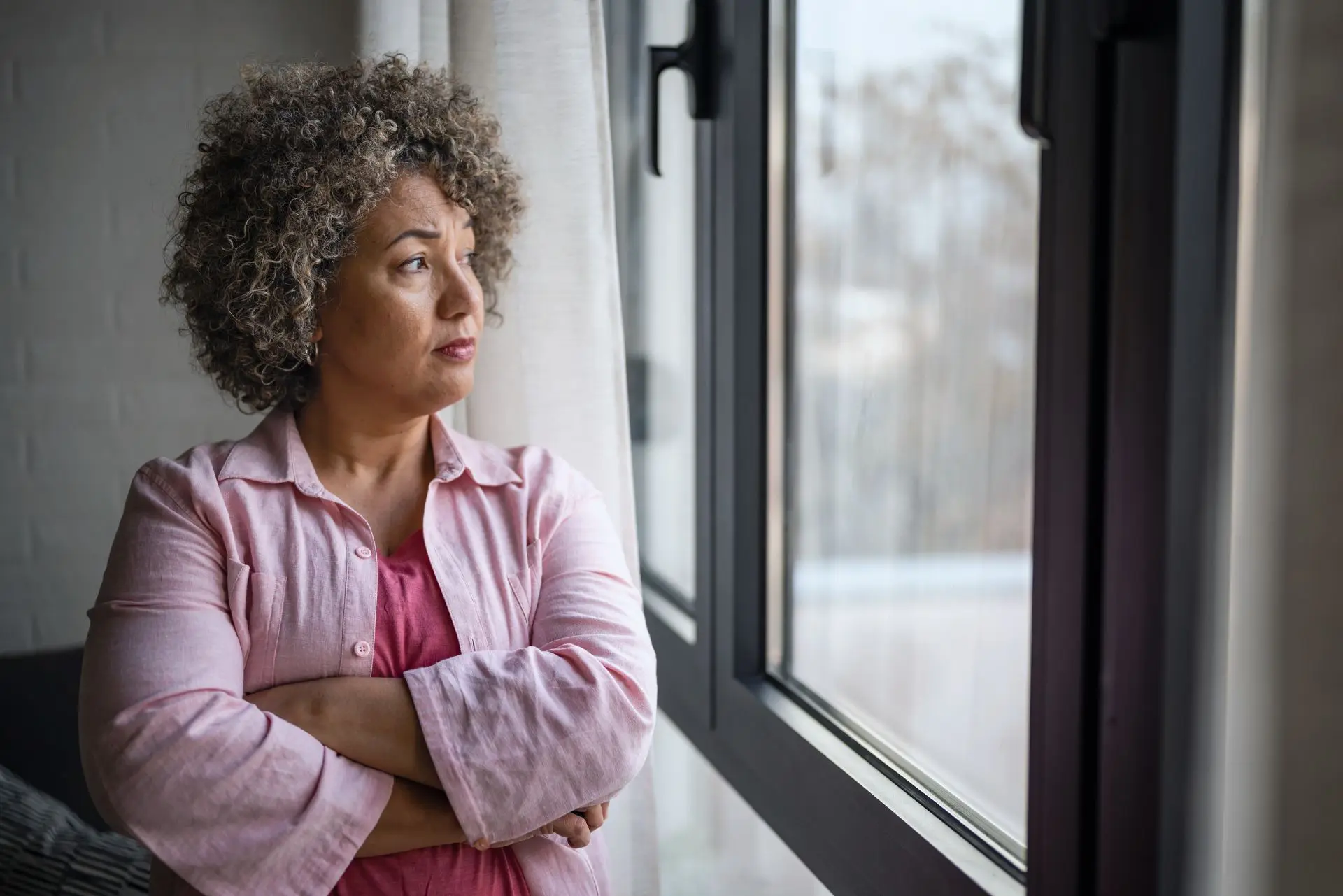 Croyances limitantes : une femme réfléchit face à la fenêtre, confrontée à des pensées qui peuvent freiner sa confiance et ses projets.
