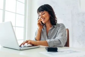 Préparer sa rentrée professionnelle : une femme souriante travaille sur son ordinateur pour organiser sa reprise.